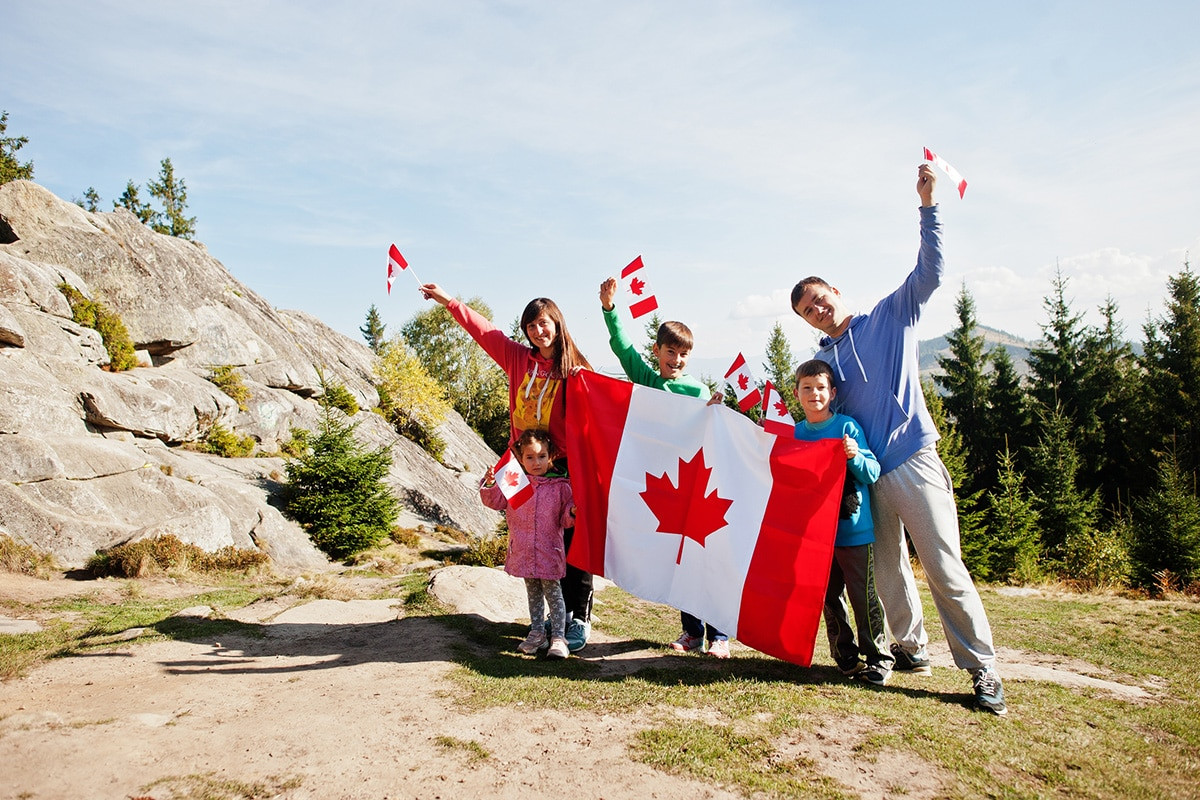 A Canadian family posing with the national flag - Canadian citizenship for foreign born citizens