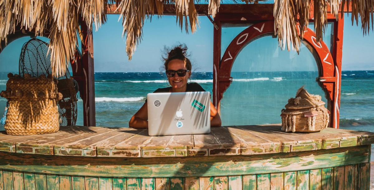 A woman sitting on tiki bar is working on laptop - Rise of Digital Nomad Lifestyle