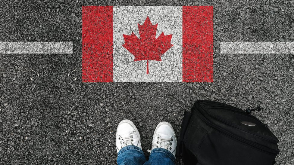 A man with shoes standing next to Canadian flag -Immigration, Population Growth and Workforce Canada